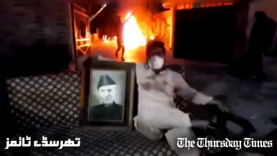 A file photo is shown of a rioter holding a photo of Mohammad Ali Jinnah as the former Corps Commanders' House at Lahore is engulfed in flames on May 9, 2023. — FILE/THE THURSDAY TIMES
