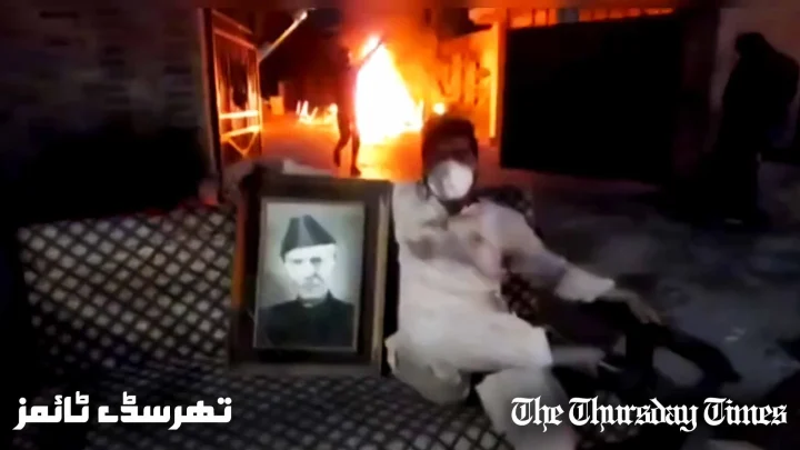 A file photo is shown of a rioter holding a photo of Mohammad Ali Jinnah as the former Corps Commanders' House at Lahore is engulfed in flames on May 9, 2023. — FILE/THE THURSDAY TIMES