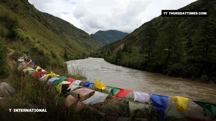 Buddhist prayer flags strung along a swollen river in a green Bhutanese valley