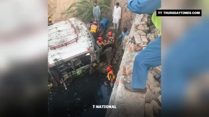 Rescue workers in orange uniforms work beside an overturned bus lying in a drain