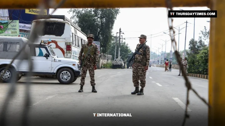 Two armed security personnel stand on an empty road behind a barrier in Imphal