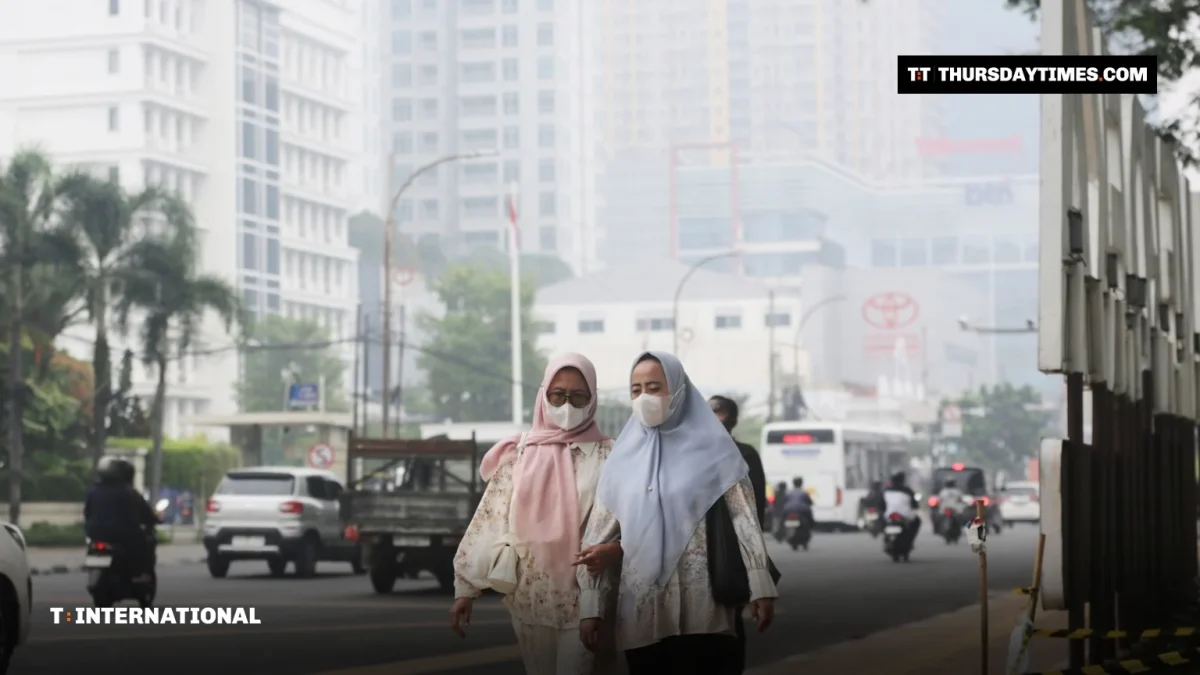 Two women wearing face masks walk along a street shrouded in haze in Jakarta