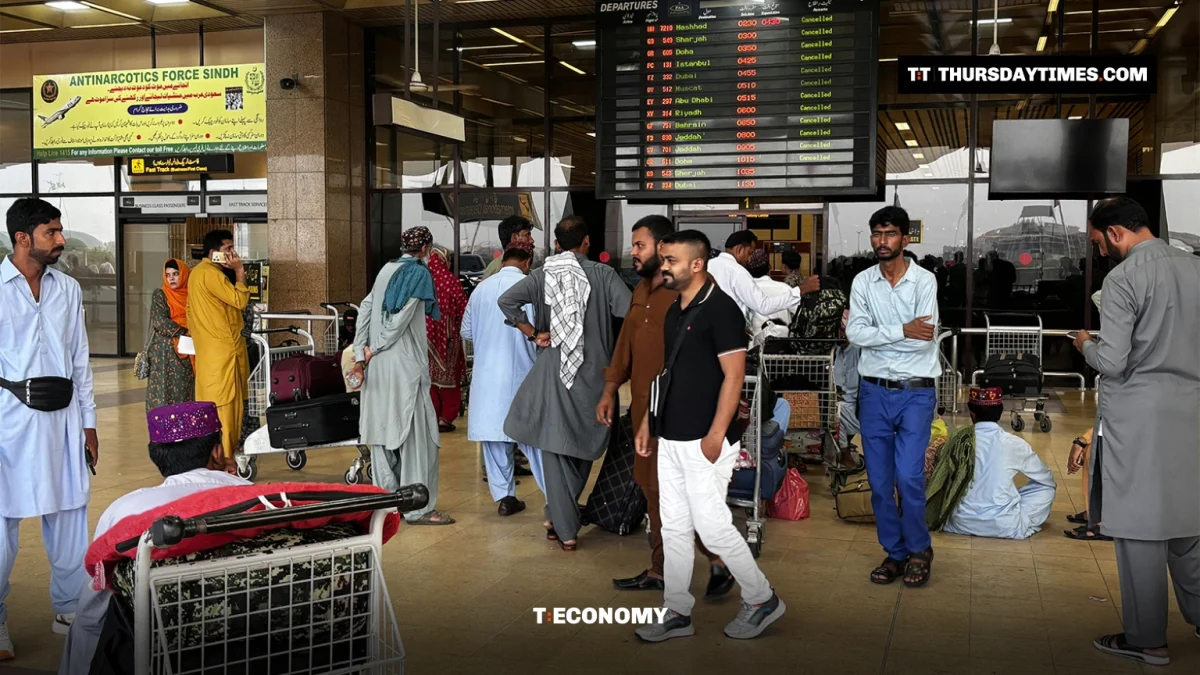 Passengers with luggage trolleys stand beneath a departures board in the terminal at Karachi airport