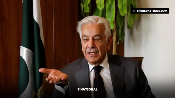 Khawaja Asif gestures during an interview beside a Pakistani flag