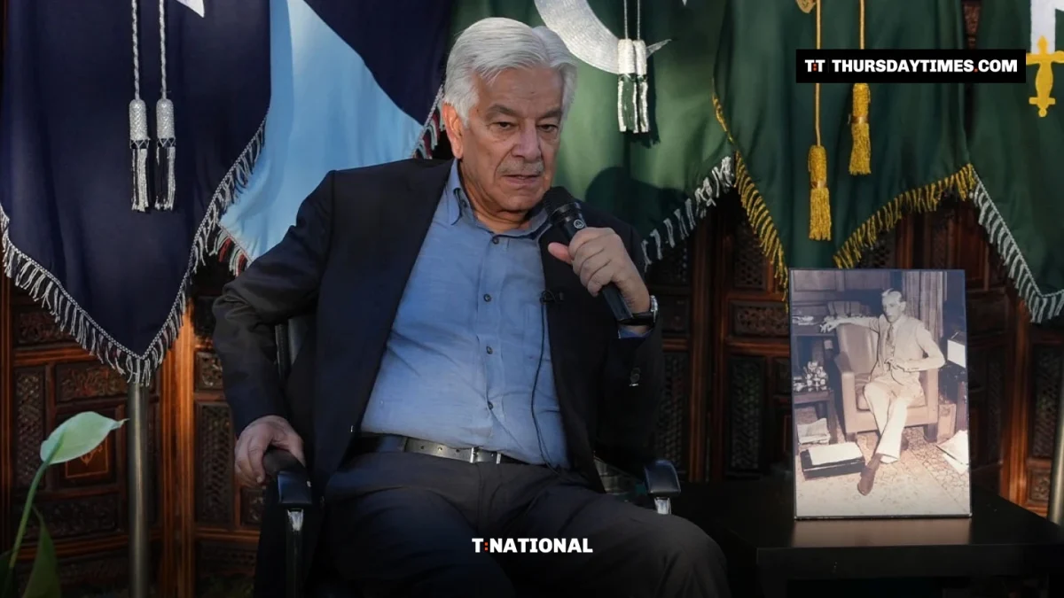Khawaja Asif speaks into a microphone in front of Pakistani flags
