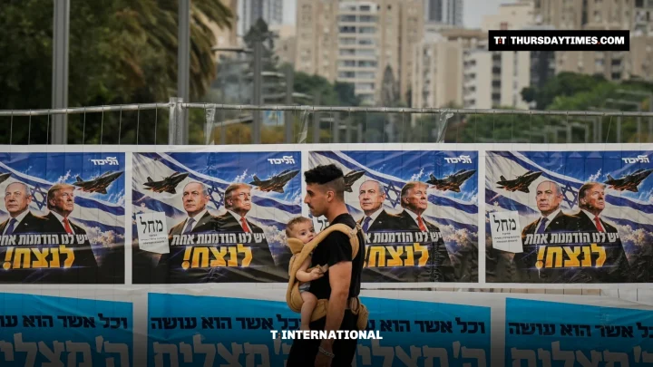 A man carrying a child walks past Likud campaign banners showing Netanyahu and Trump