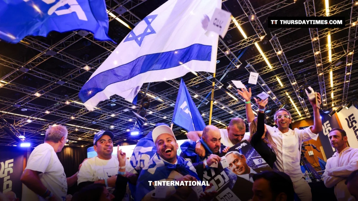 Likud supporters cheer and wave Israeli and party flags under stage lights at the party headquarters