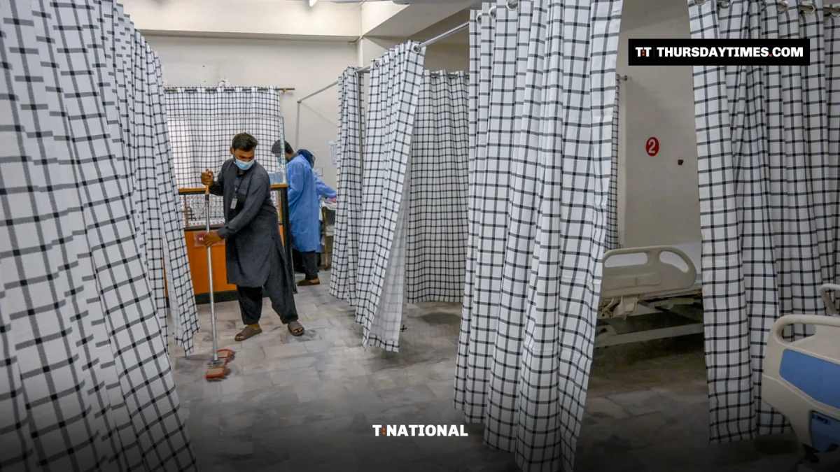 A masked worker mops the floor between curtained beds in a hospital isolation ward