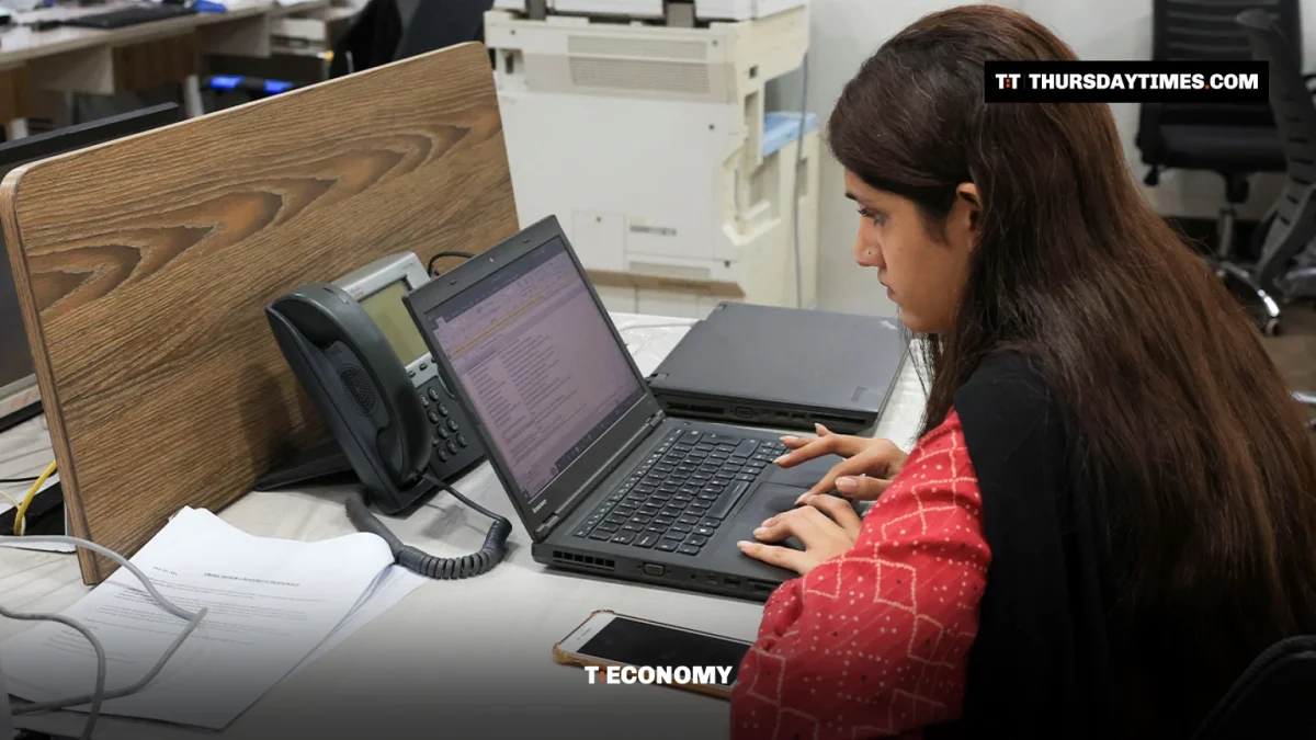 A woman in a red kameez types on a laptop at an office desk in Karachi