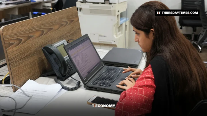 A woman in a red kameez types on a laptop at an office desk in Karachi