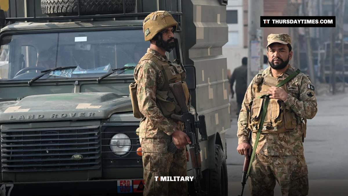 Two armed Pakistani soldiers in helmets stand beside a military vehicle in Peshawar