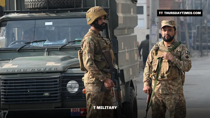 Two armed Pakistani soldiers in helmets stand beside a military vehicle in Peshawar