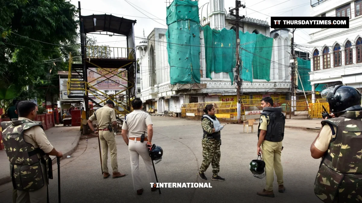 Police officers stand in an empty street in front of a mosque covered in green netting