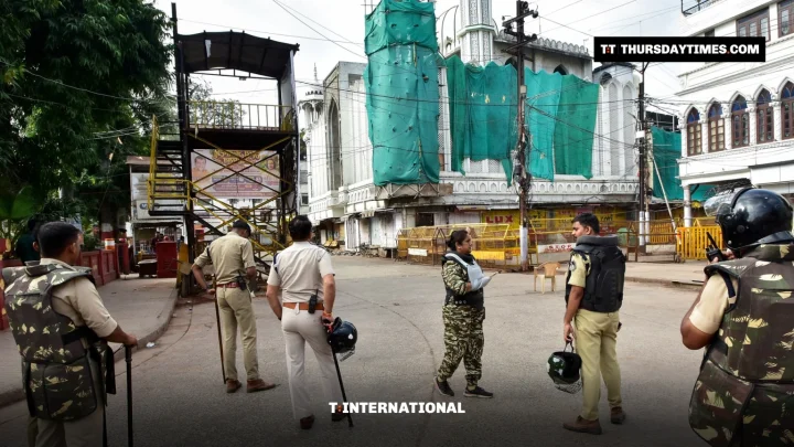 Police officers stand in an empty street in front of a mosque covered in green netting