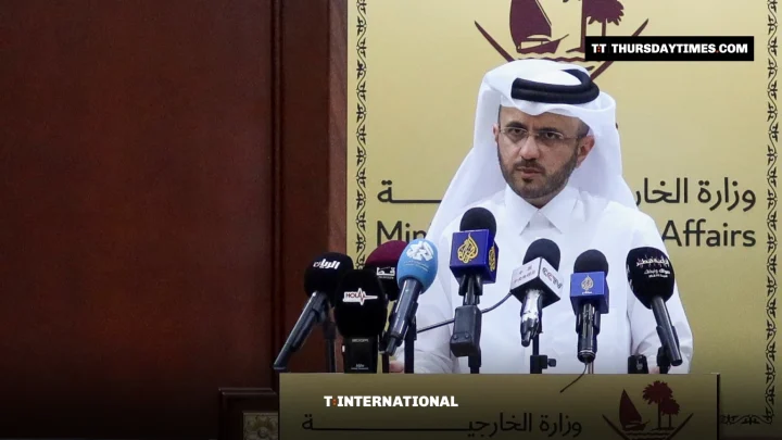 Majed al-Ansari in white thobe and ghutra speaks at a podium with broadcasters’ microphones at Qatar’s Foreign Ministry