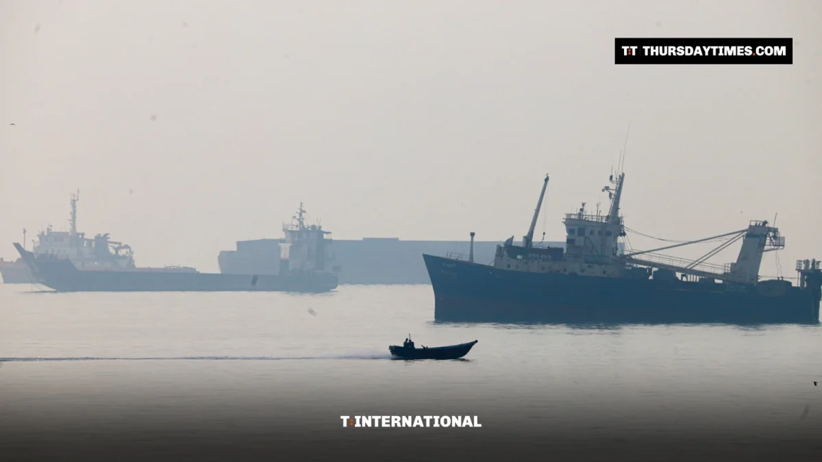 A small motorboat speeds past large commercial vessels anchored in a hazy Strait of Hormuz
