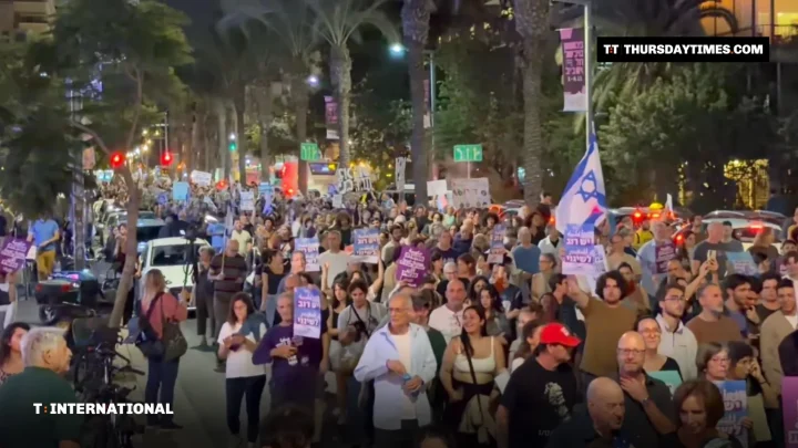A large crowd marches with placards and Israeli flags along a palm-lined street in Tel Aviv at night
