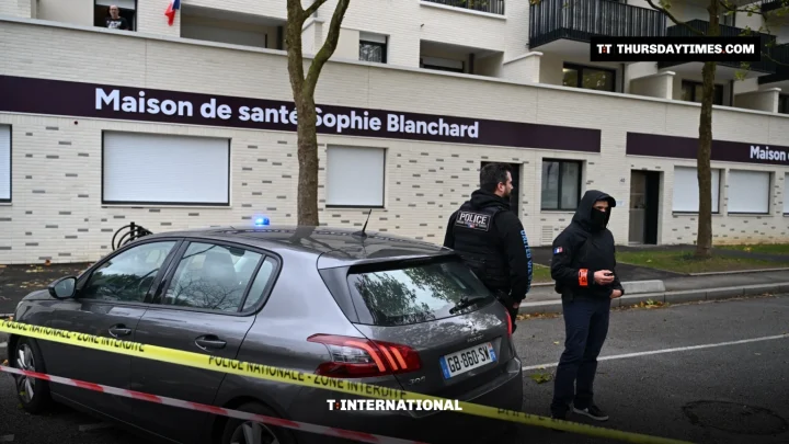Two French police officers stand by a police car behind cordon tape outside a health centre in Trappes