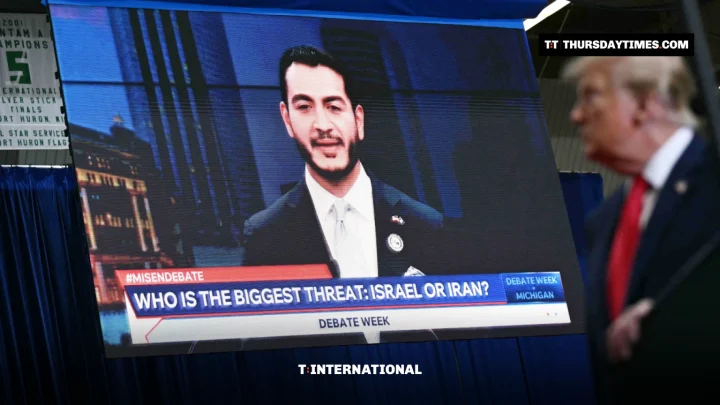 A large screen shows Abdul El-Sayed during a debate broadcast while Donald Trump, in the foreground, speaks at a rally