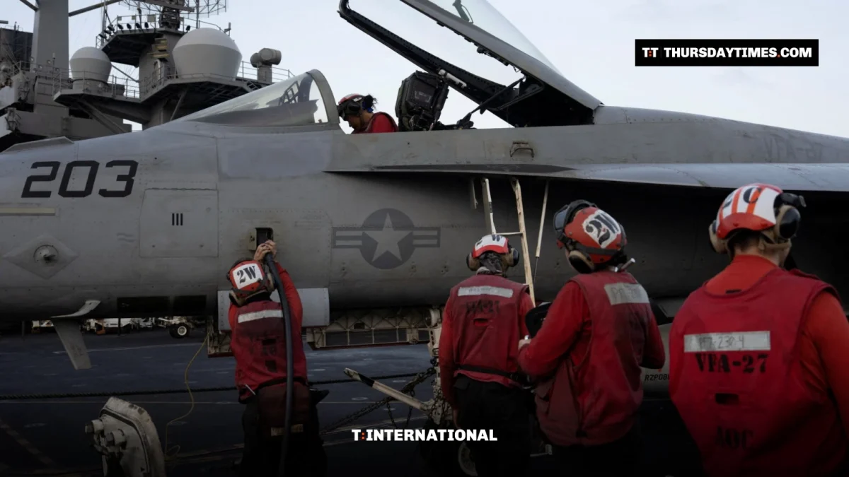 Sailors in red jerseys work around an F/A-18 fighter jet on an aircraft carrier deck
