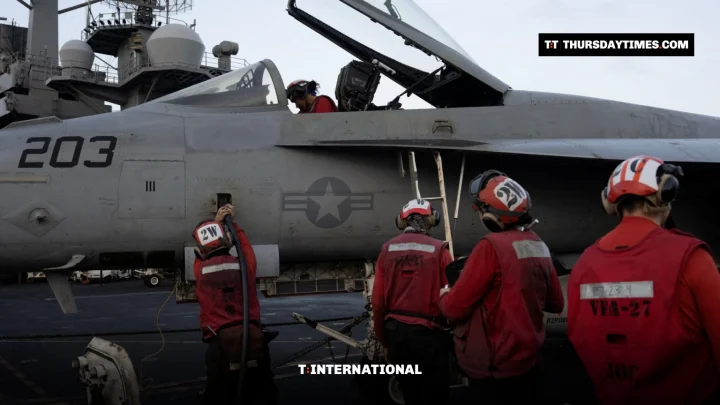 Sailors in red jerseys work around an F/A-18 fighter jet on an aircraft carrier deck