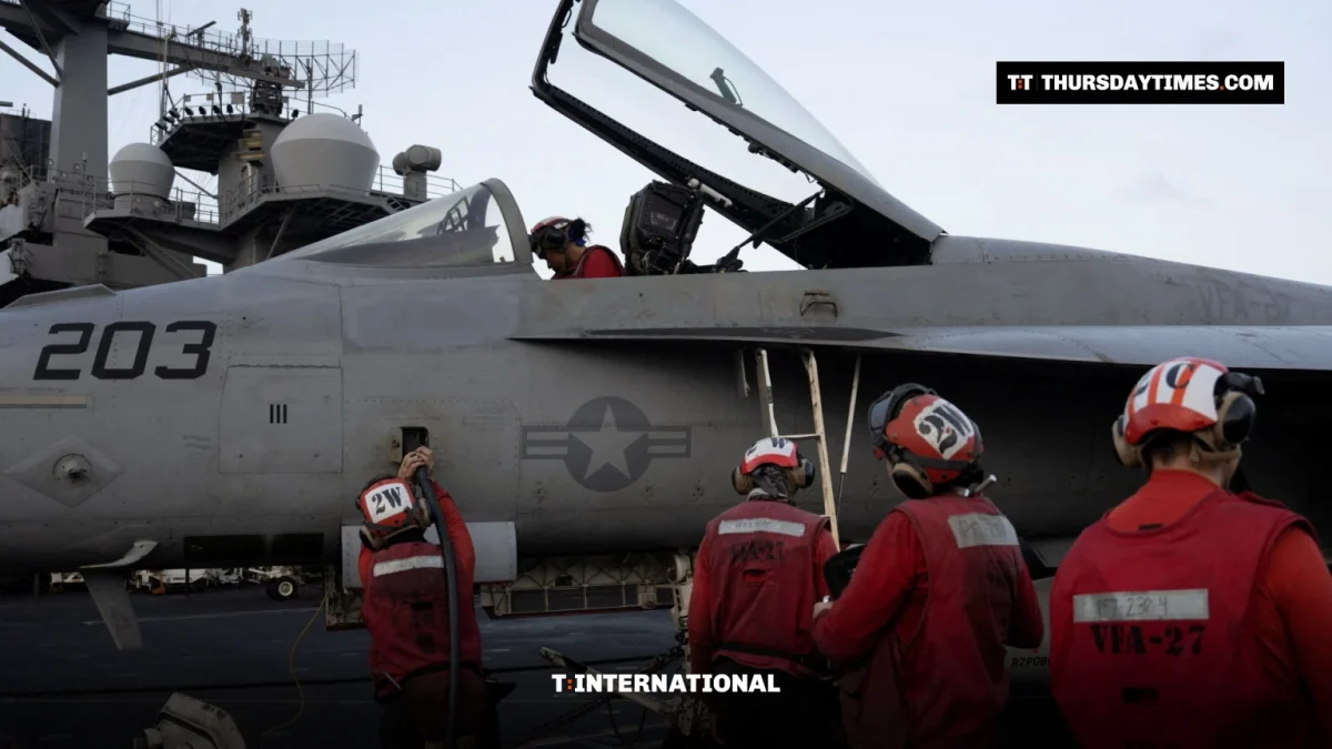 Sailors in red jerseys work around a grey US Navy fighter jet on an aircraft carrier deck