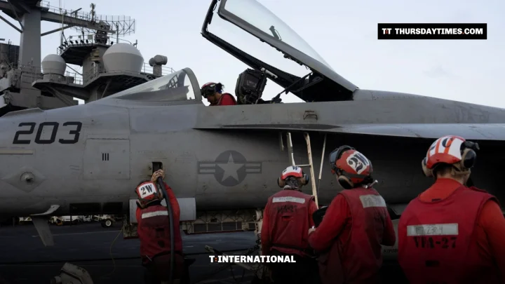Sailors in red jerseys work around a grey US Navy fighter jet on an aircraft carrier deck