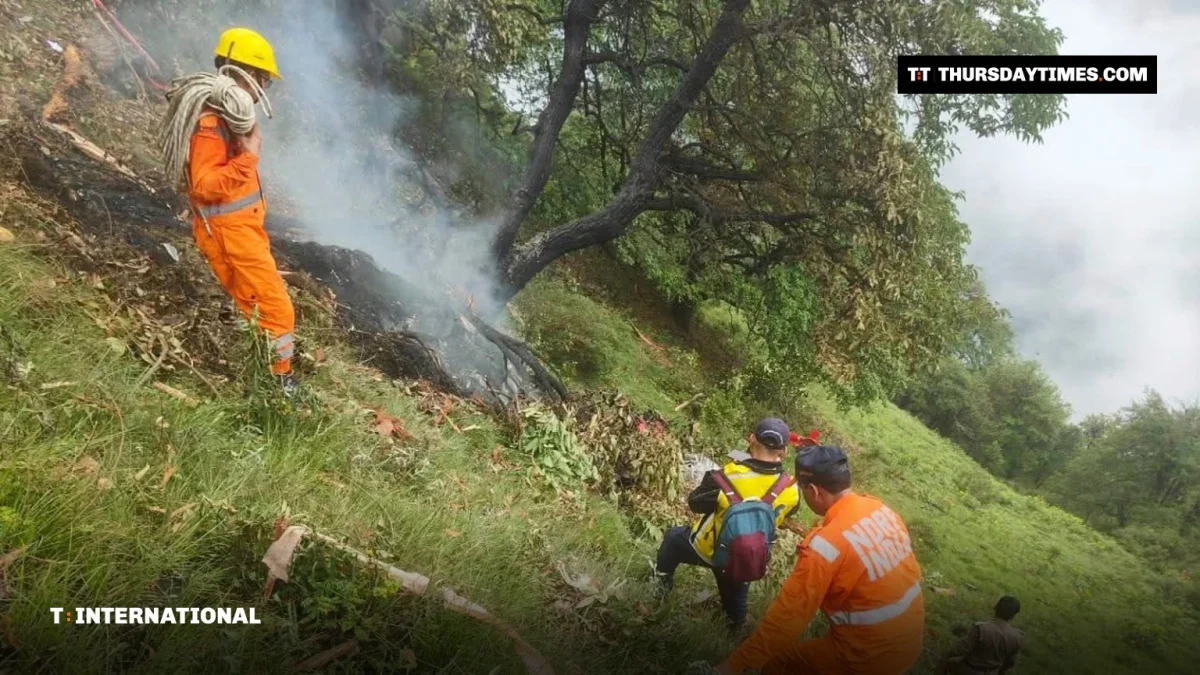 Rescue workers in orange uniforms at a smouldering helicopter crash site on a forested hillside