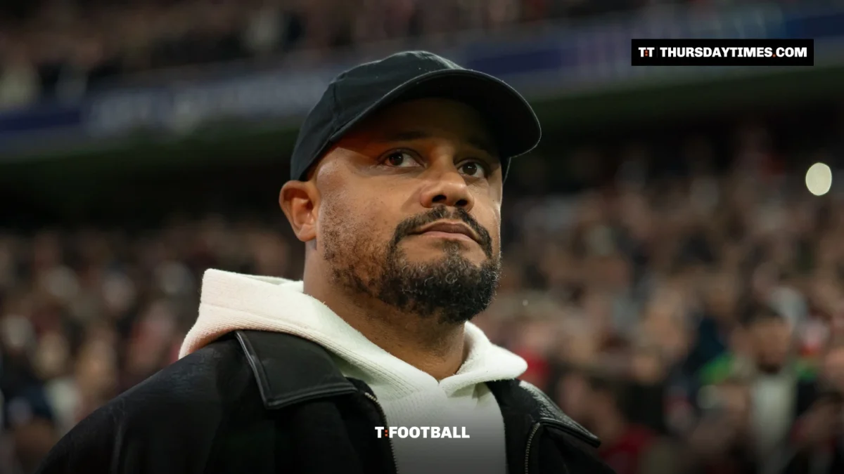 Vincent Kompany in a black cap and white hoodie on the touchline at a packed stadium