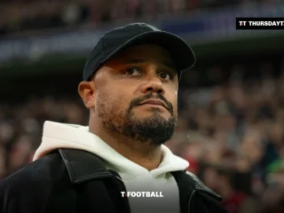 Vincent Kompany in a black cap and white hoodie on the touchline at a packed stadium