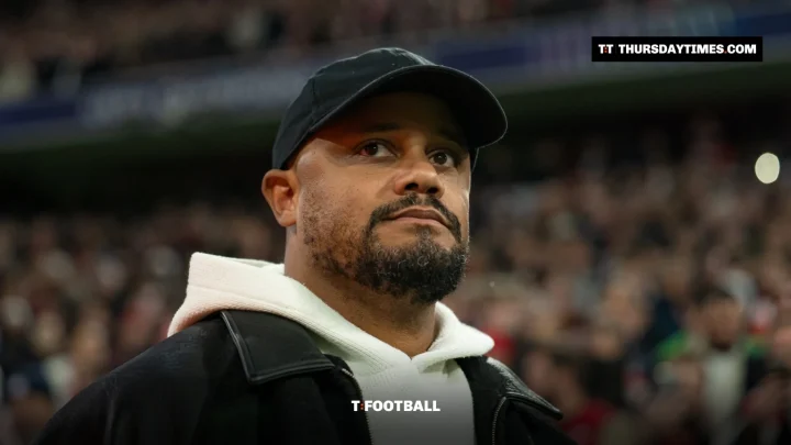 Vincent Kompany in a black cap and white hoodie on the touchline at a packed stadium